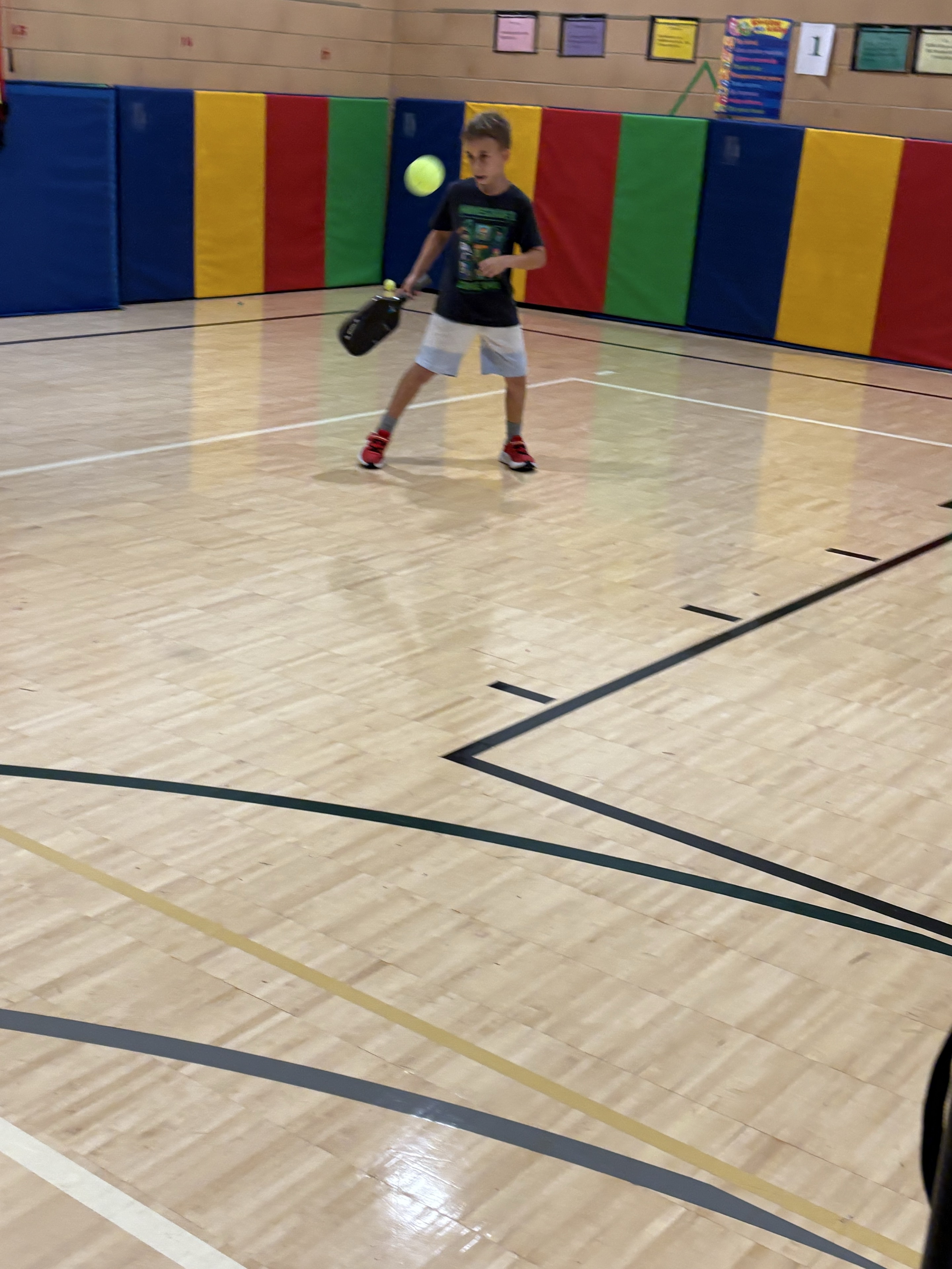 A young player returning a ball in a gym